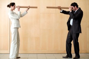 Businessman and businesswoman looking at each other through cardboard tubes. Horizontal shot.